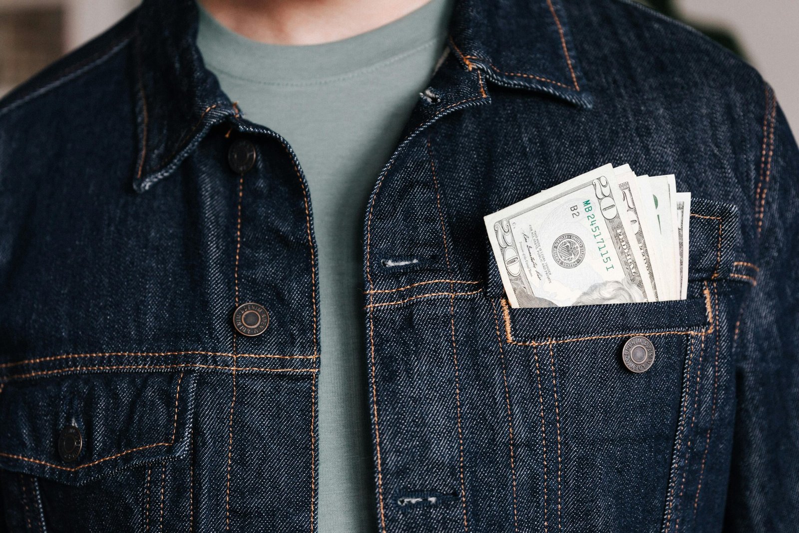Crop unrecognizable male in casual outfit standing with different nominal pars of dollar banknotes in pocket of jeans jacket