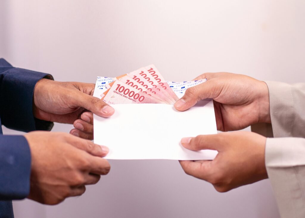 Hands exchanging an envelope with Indonesian Rupiah, highlighting financial transactions.