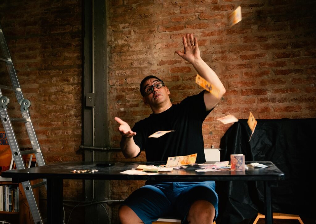 Man tossing bills playfully on an indoor table against a rustic brick wall.