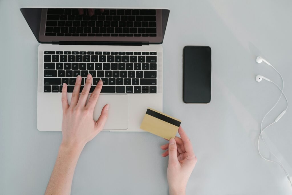 Flat lay of a workspace with a laptop, bank card, smartphone, and earphones, ideal for online finance themes.