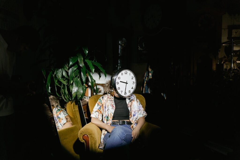 A unique portrait of a person with a clock as a head, seated in a dimly lit room with houseplants.